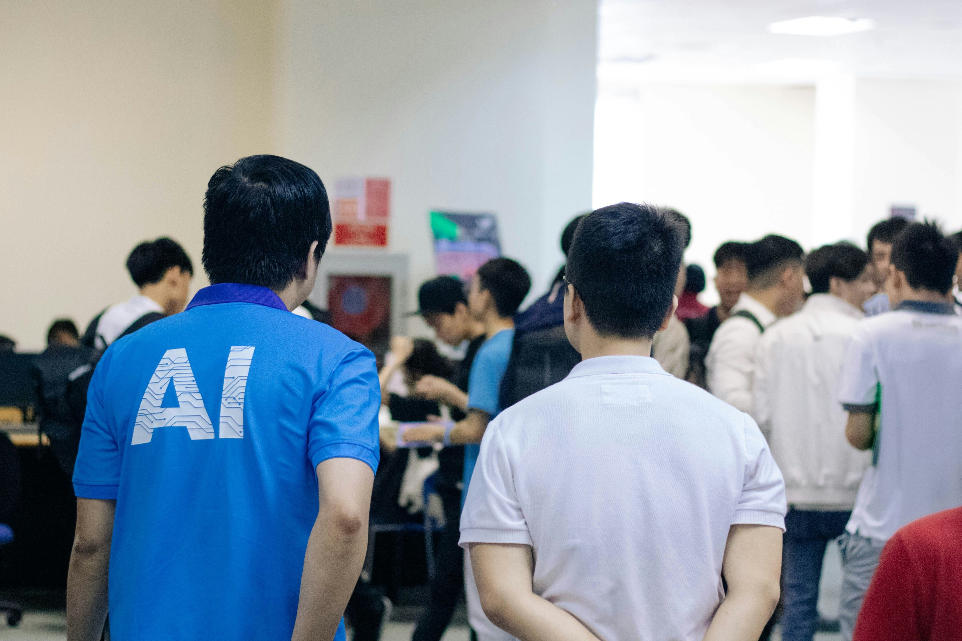 Students in a classroom. One wearing a shirt with AI on the back